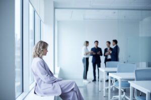Mujer sentada al margen de una reunión, mira a un lado mientras el grupo conversa, imagen del ninguneo y la invisibilidad