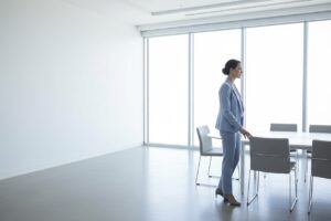 Mujer de pie a un lado de una sala de reuniones luminosa, símbolo de quien tiene el cargo pero no consigue ganar influencia en el trabajo